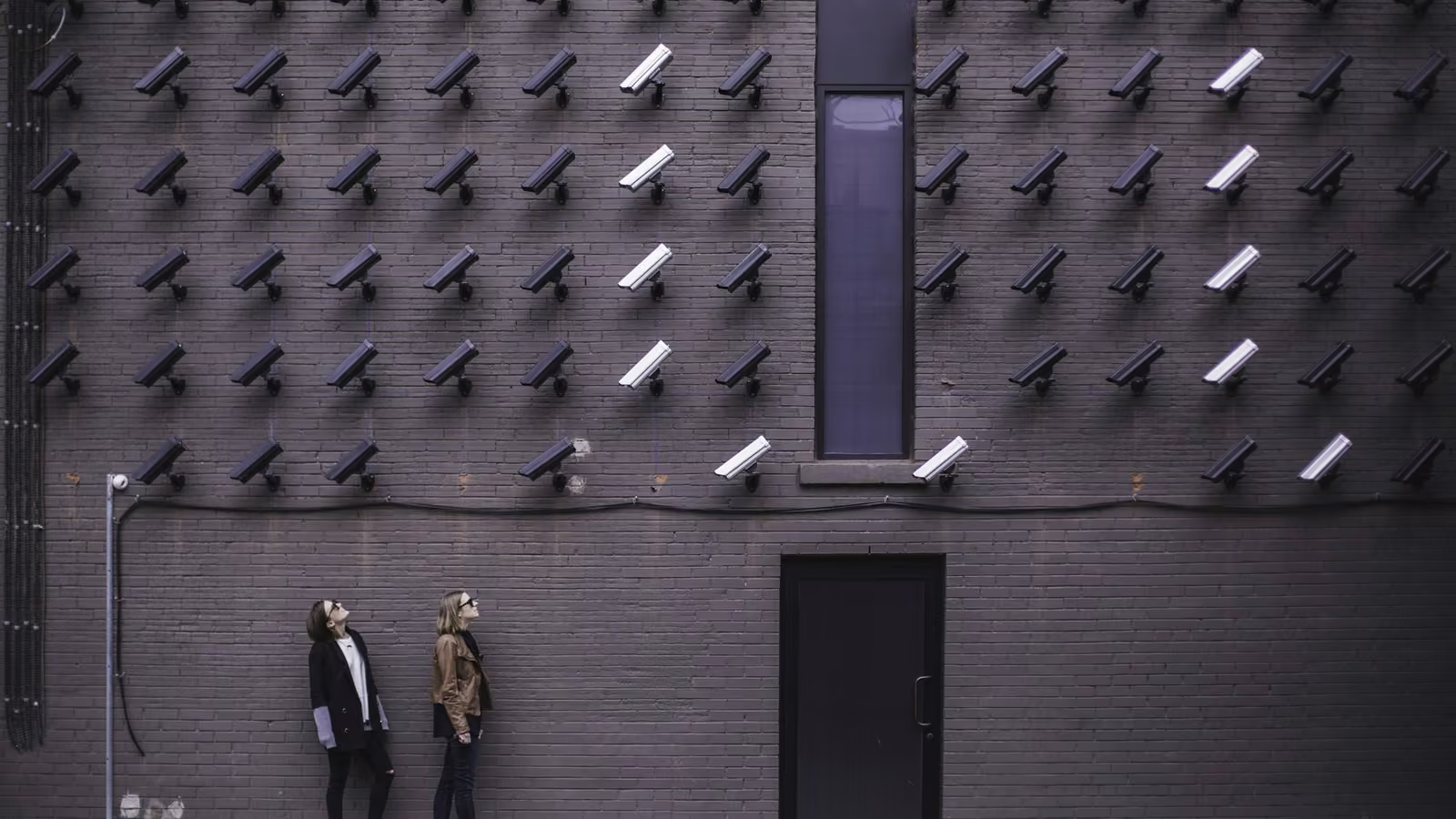 Muro cubierto de cámaras de videovigilancia observado por dos personas