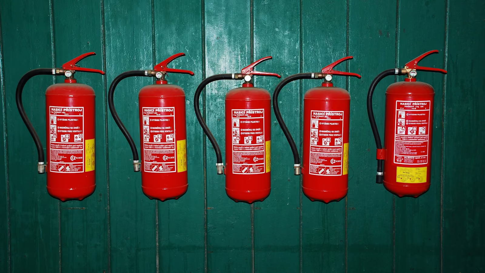 Hilera de extintores rojos montados en una pared verde