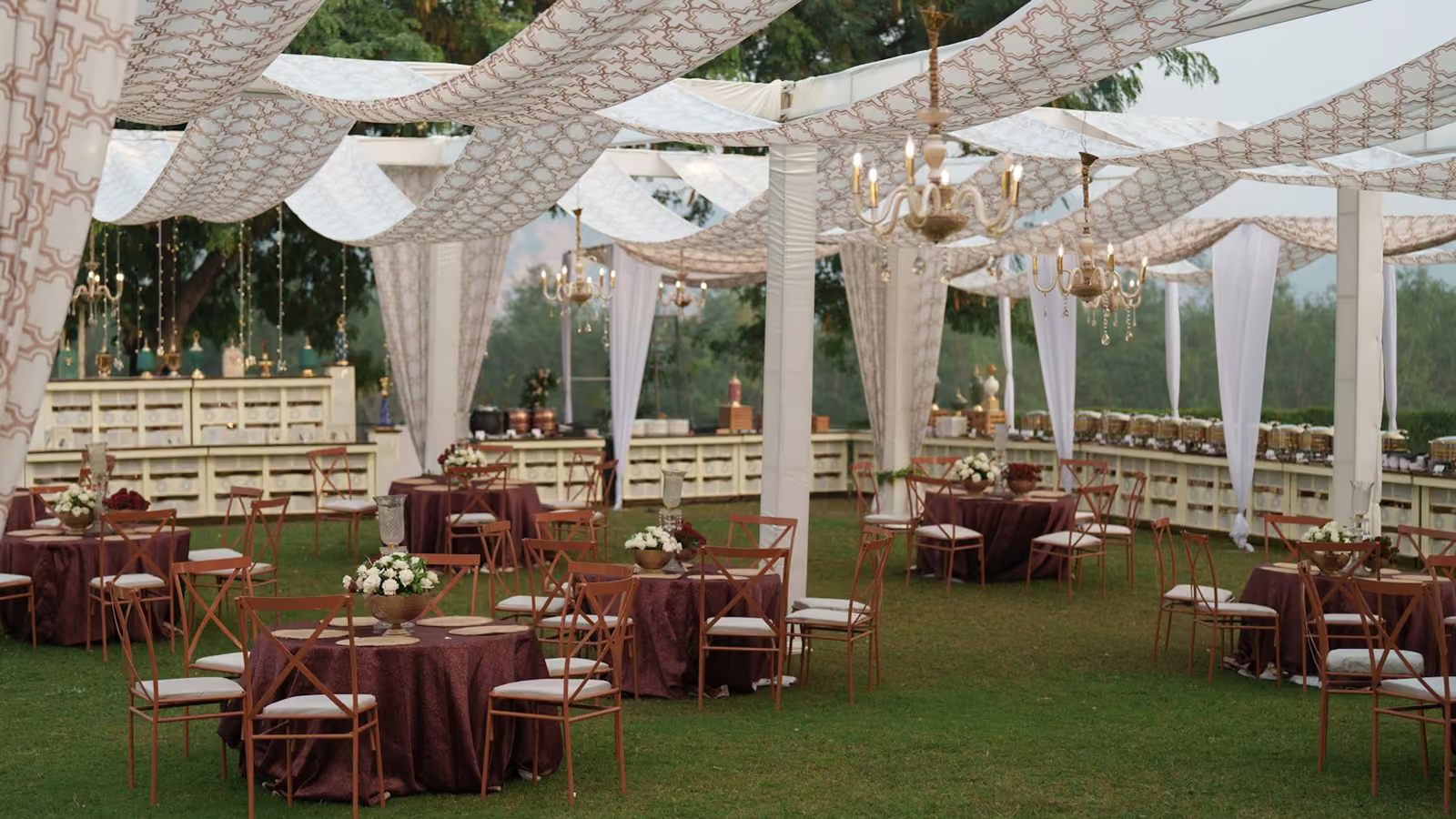 Carpa con cortinas blancas y mesas montadas para una boda al aire libre