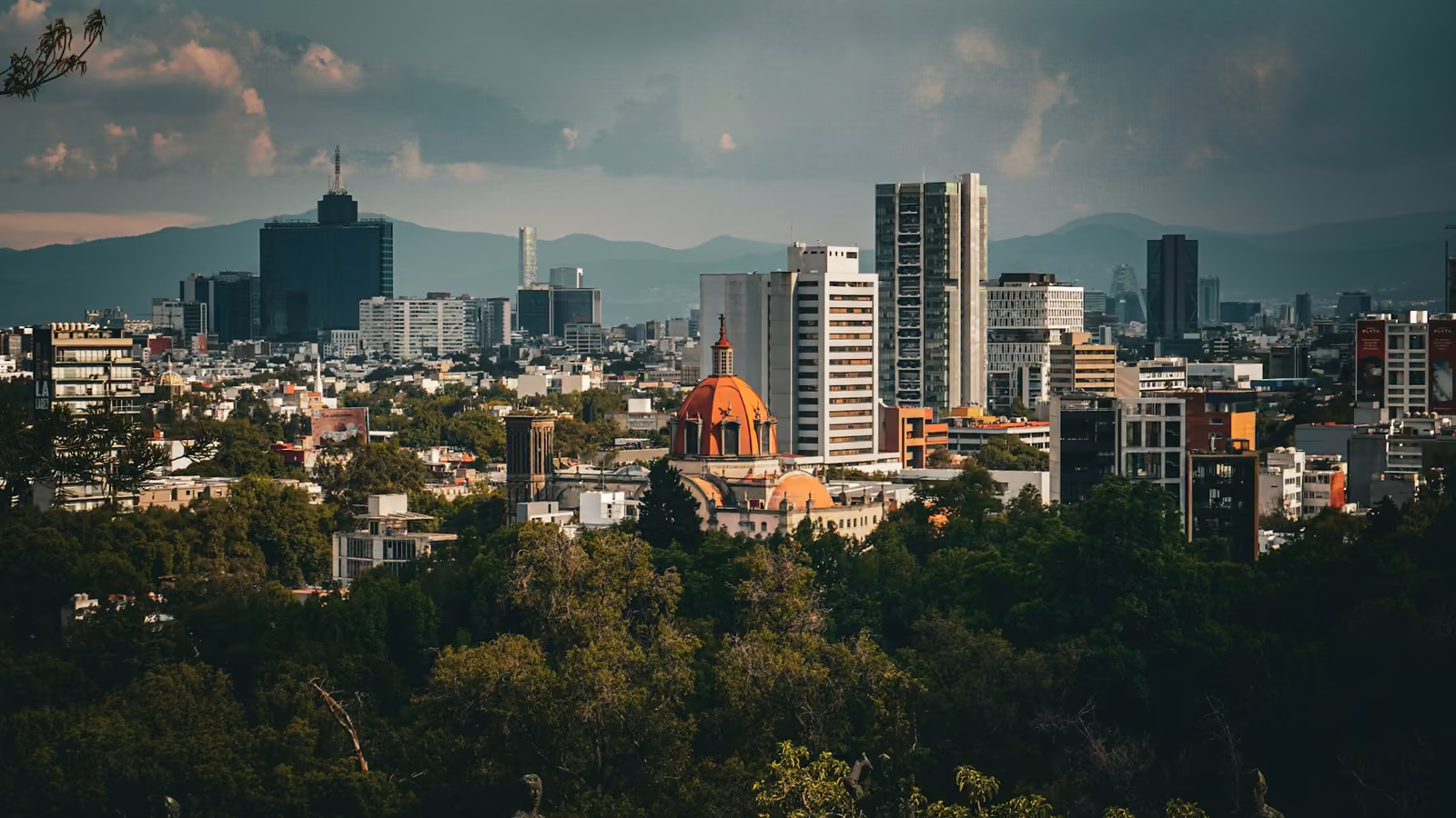 Vista de la Ciudad de México con la cúpula de una iglesia entre edificios y árboles
